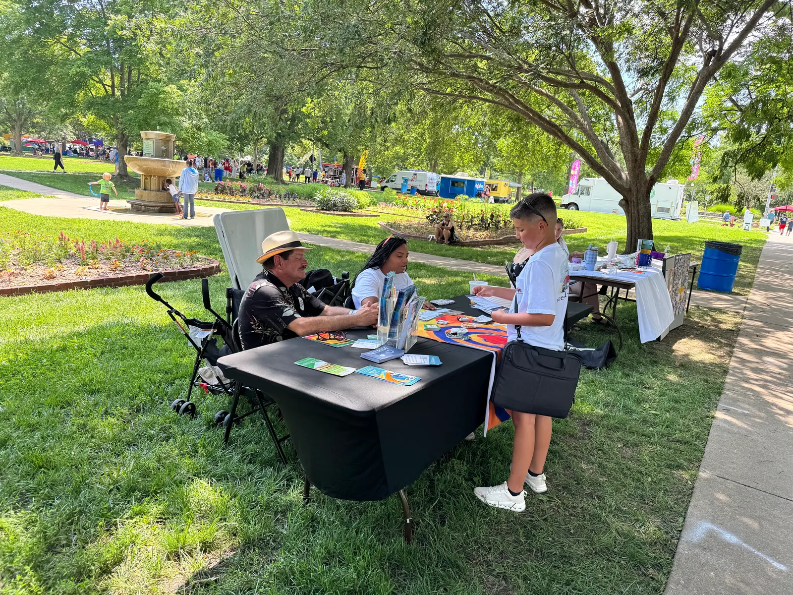 Constituents talk with a campaign volunteer at an outreach table in a Lawrence park on Juneteenth.